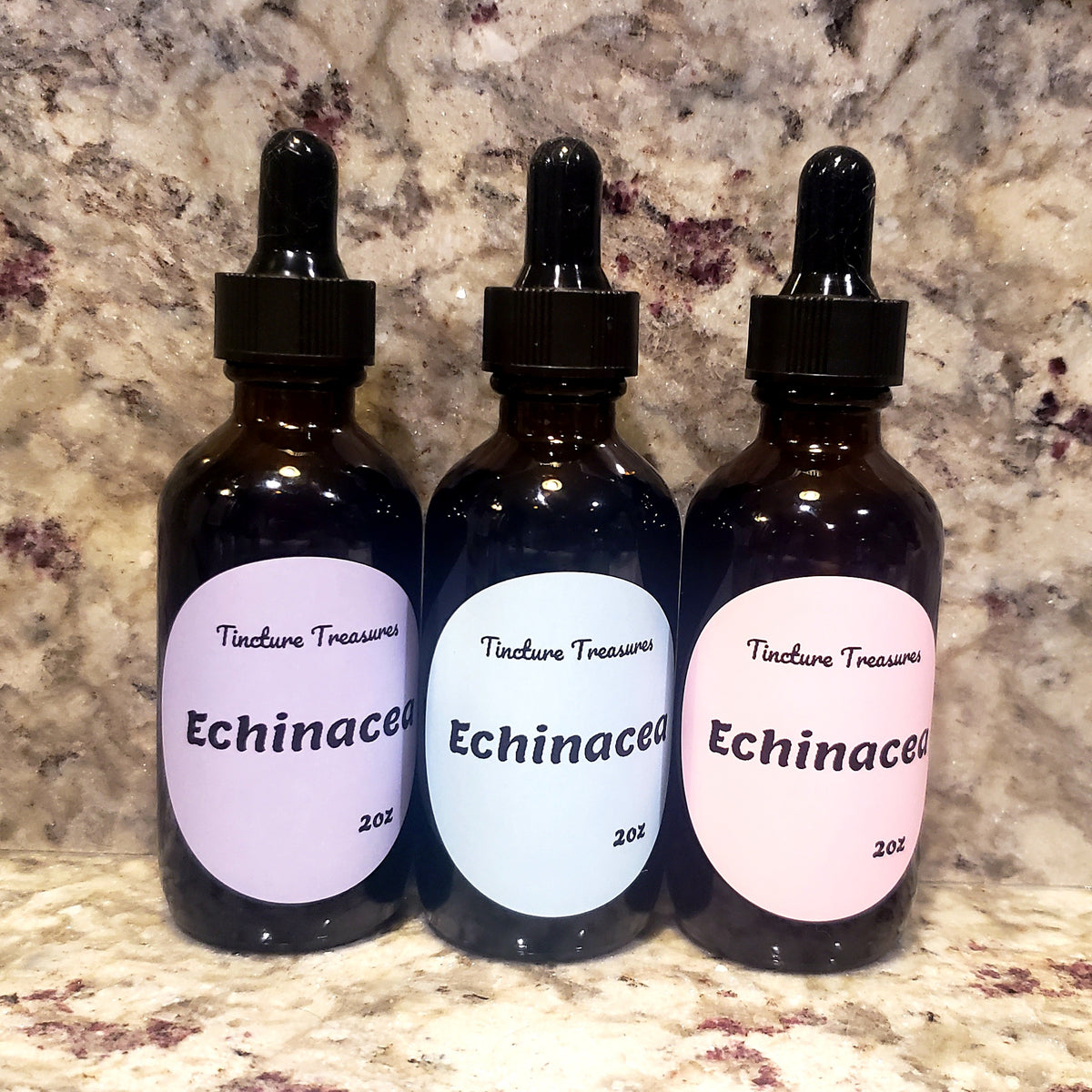 Three amber glass dropper bottles labeled 'Tincture Treasures Echinacea' with lavender, light blue, and pale pink labels, set against a mottled stone countertop.