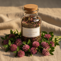 Red clover herbal tea in a glass jar with vibrant red clover blossoms on a warm linen surface